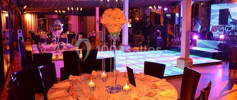 Salle de réception décorée avec des tables élégantes, un éclairage coloré et une piste de danse illuminée.