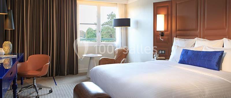 Chambre d'hôtel lumineuse avec un grand lit, un bureau, un fauteuil, une table ronde et une fenêtre donnant sur un espace…