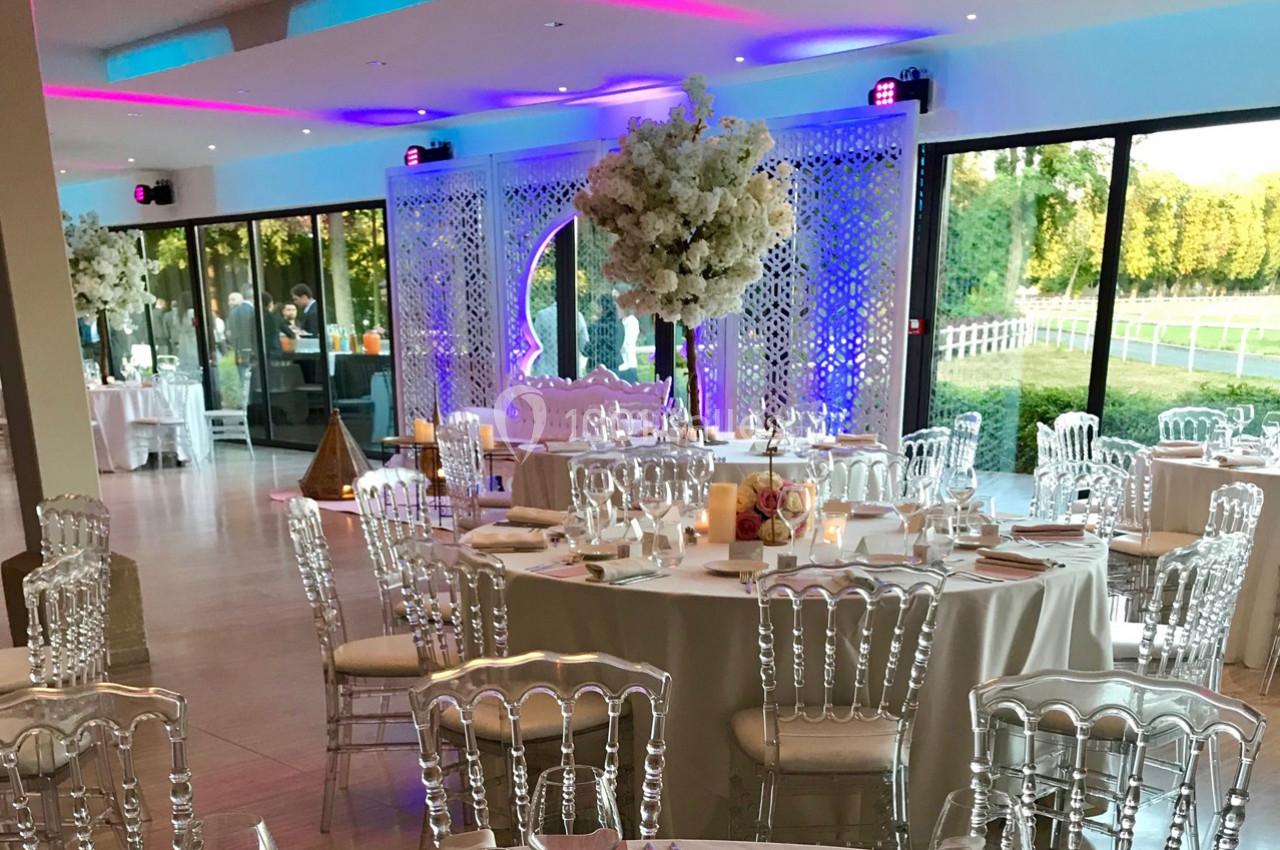 Salle de réception décorée avec des tables élégantes, des chaises transparentes et des arrangements floraux blancs.