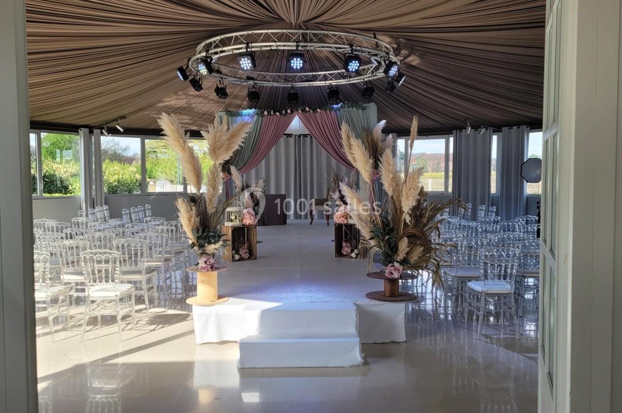 Salle de réception décorée avec des chaises transparentes, des arrangements floraux et un éclairage suspendu.