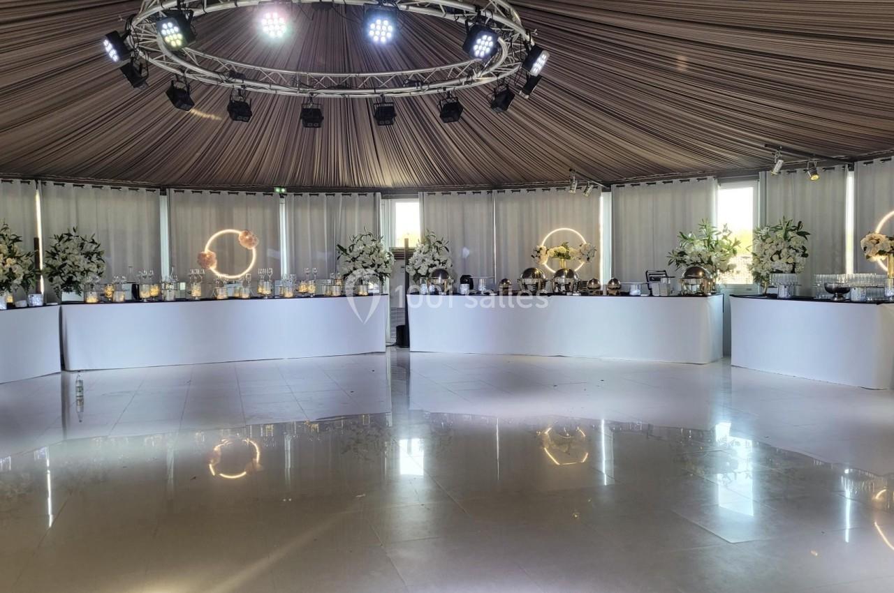 Salle de réception avec tables décorées de fleurs blanches, éclairage tamisé et plafond en tissu tendu.