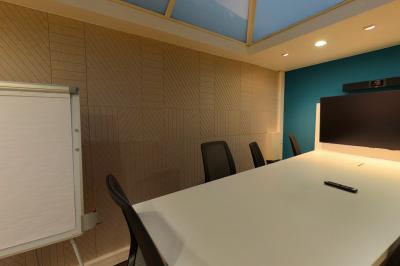 Salle de réunion moderne avec table blanche, chaises noires, mur bleu et éclairage intégré au plafond.