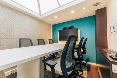Salle de réunion moderne avec table blanche, chaises noires, mur bleu et éclairage intégré au plafond.