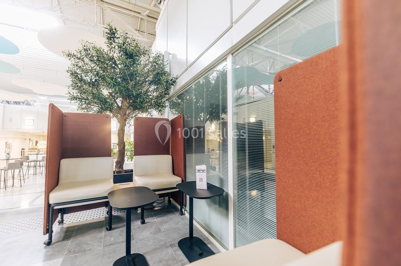 Espace de travail moderne avec sièges, tables noires, cloison en verre et arbre décoratif en intérieur lumineux.