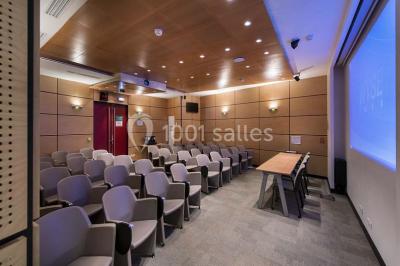 Salle de réunion moderne avec table blanche, chaises noires, mur bleu et éclairage intégré au plafond.