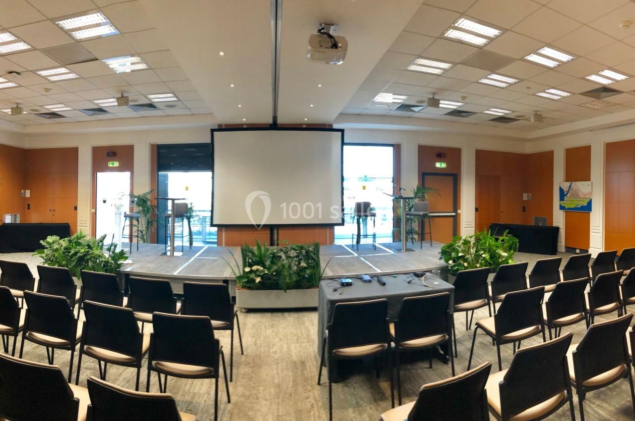 Salle de conférence lumineuse avec écran de projection, chaises alignées et plantes décoratives.
