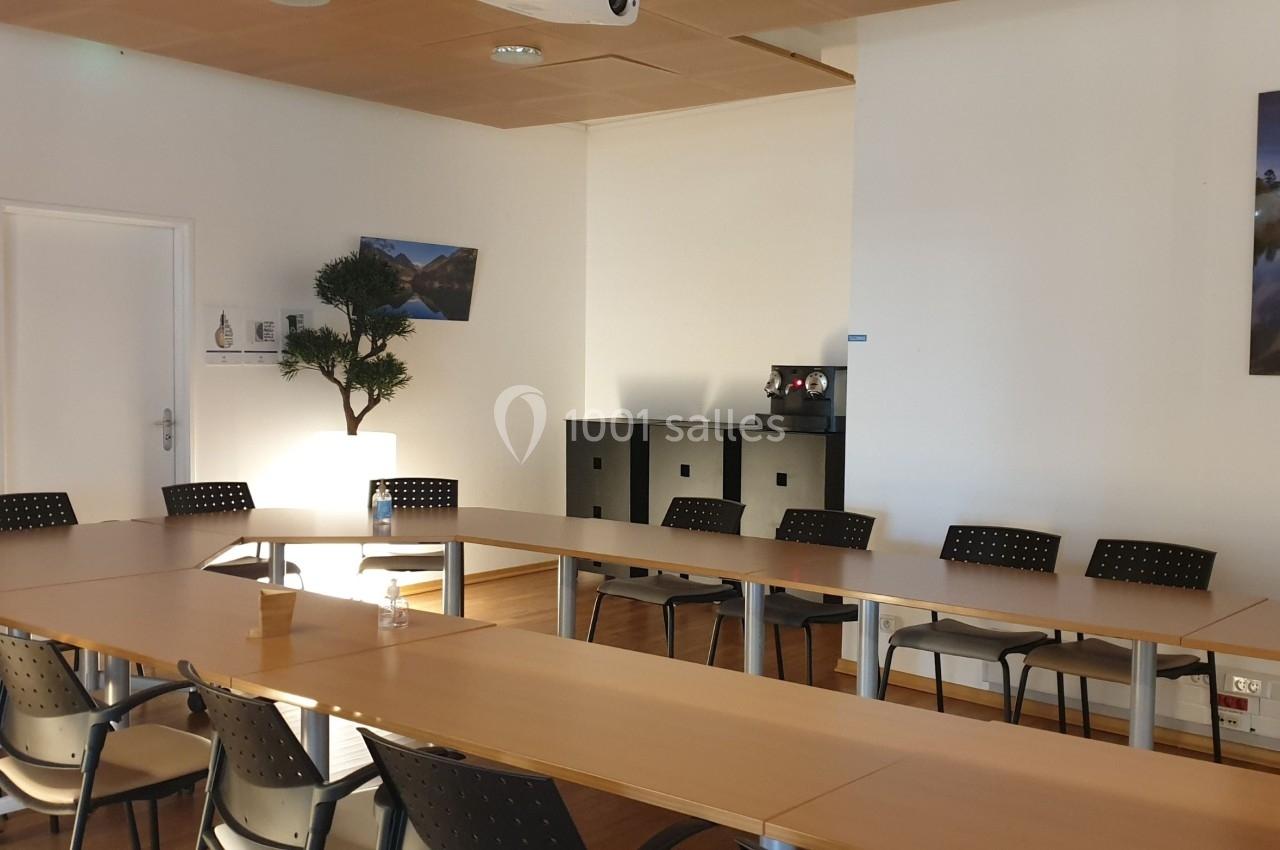 Salle de réunion lumineuse avec tables disposées en U, chaises noires, plantes et décorations murales.