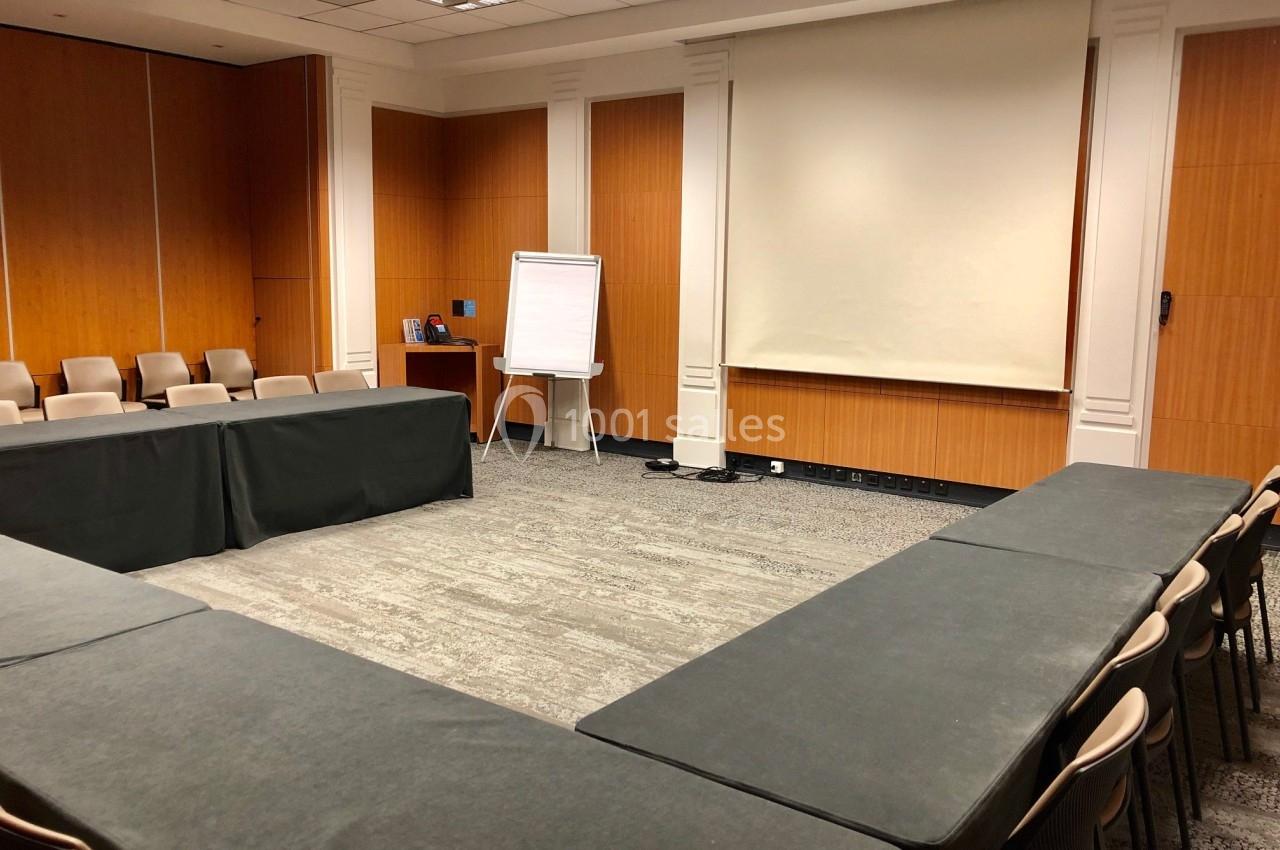 Salle de réunion avec tables disposées en U, chaises alignées, tableau blanc et écran de projection.