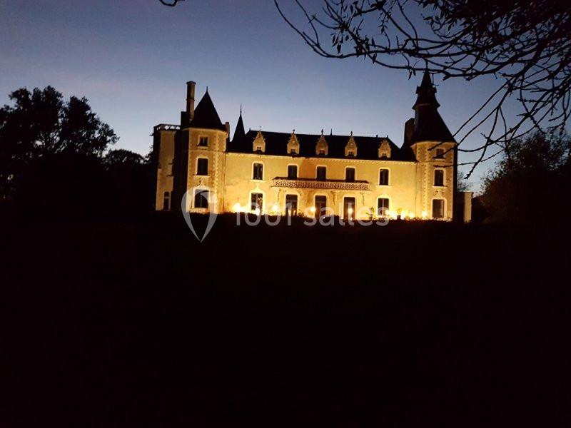 Château illuminé à la tombée de la nuit, entouré d'arbres et se détachant sur un ciel crépusculaire.