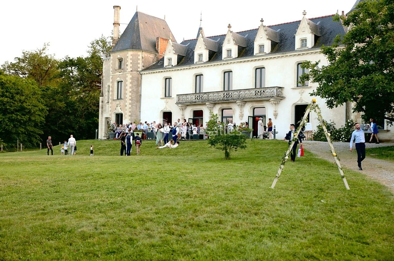 Groupe de personnes rassemblées devant un château entouré d'une pelouse et d'arbres.