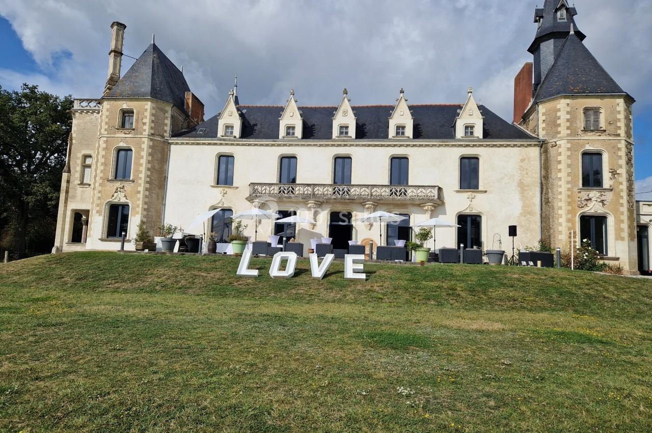 Façade d'un château avec des lettres formant le mot ’LOVE’ posées sur une pelouse devant l'entrée.