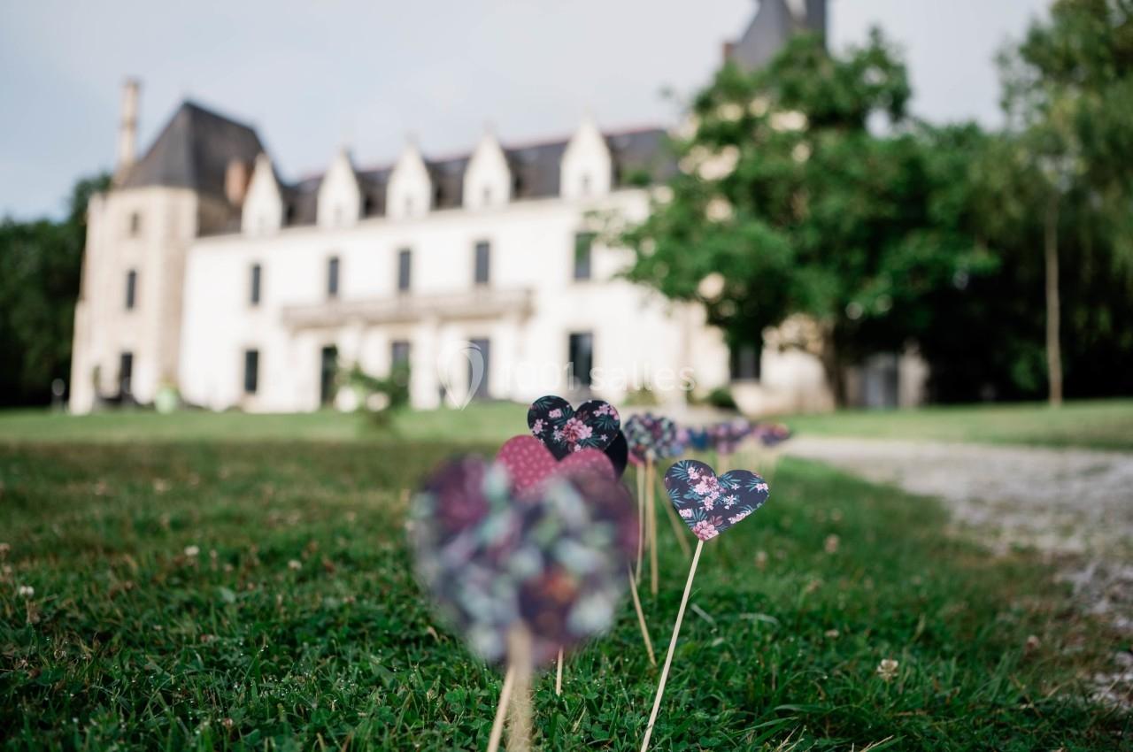 Cœurs en papier coloré plantés dans l'herbe devant un bâtiment historique entouré de verdure.