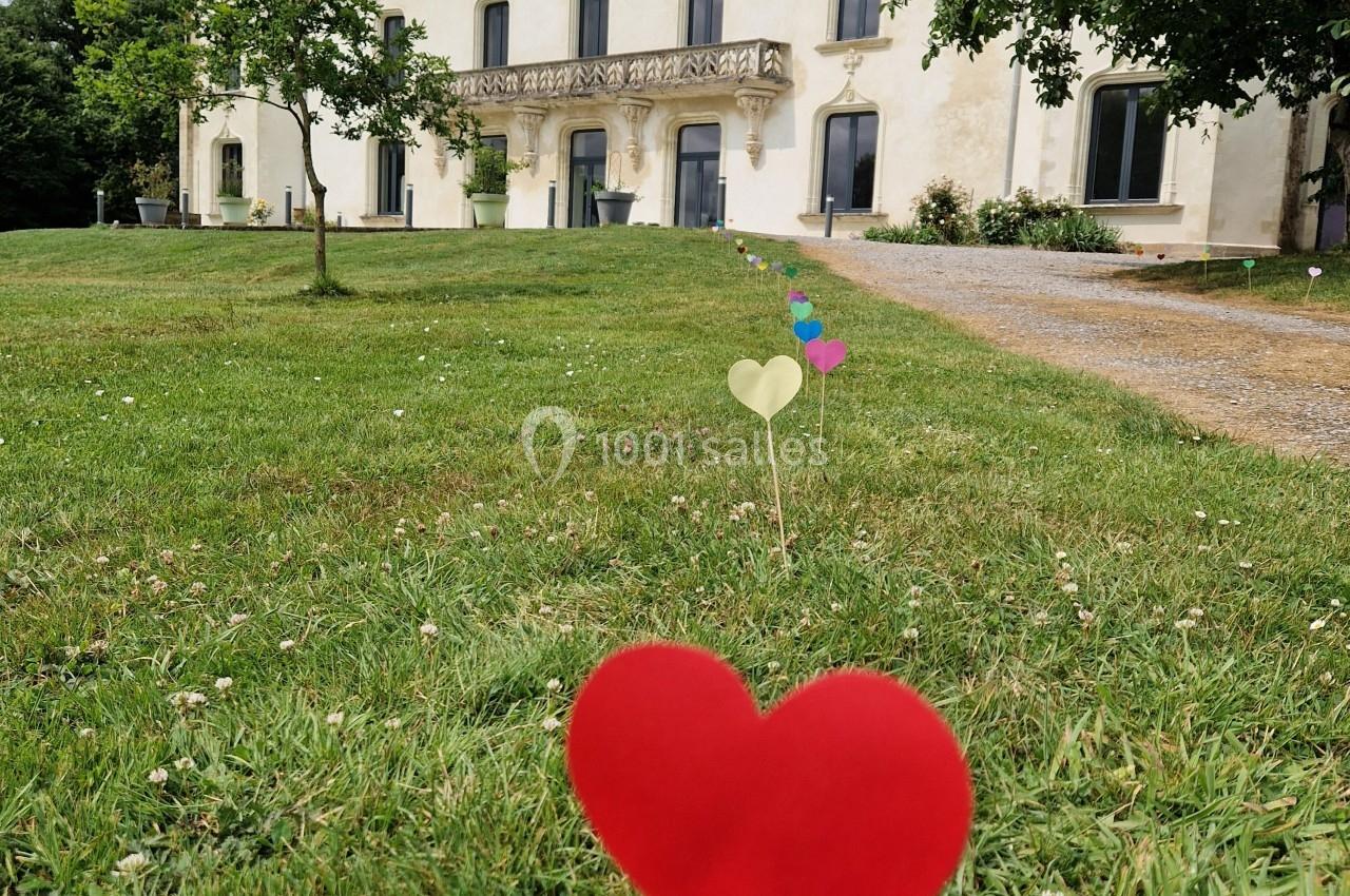 Cœurs en papier plantés dans une pelouse devant un grand bâtiment de style ancien entouré d'arbres.