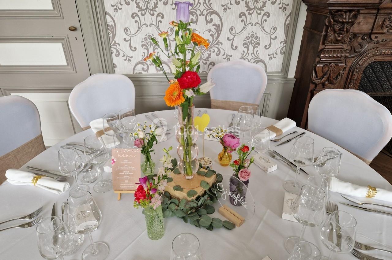 Centre de table floral coloré avec vases en verre, menu en bois et décoration élégante sur une table ronde dressée.