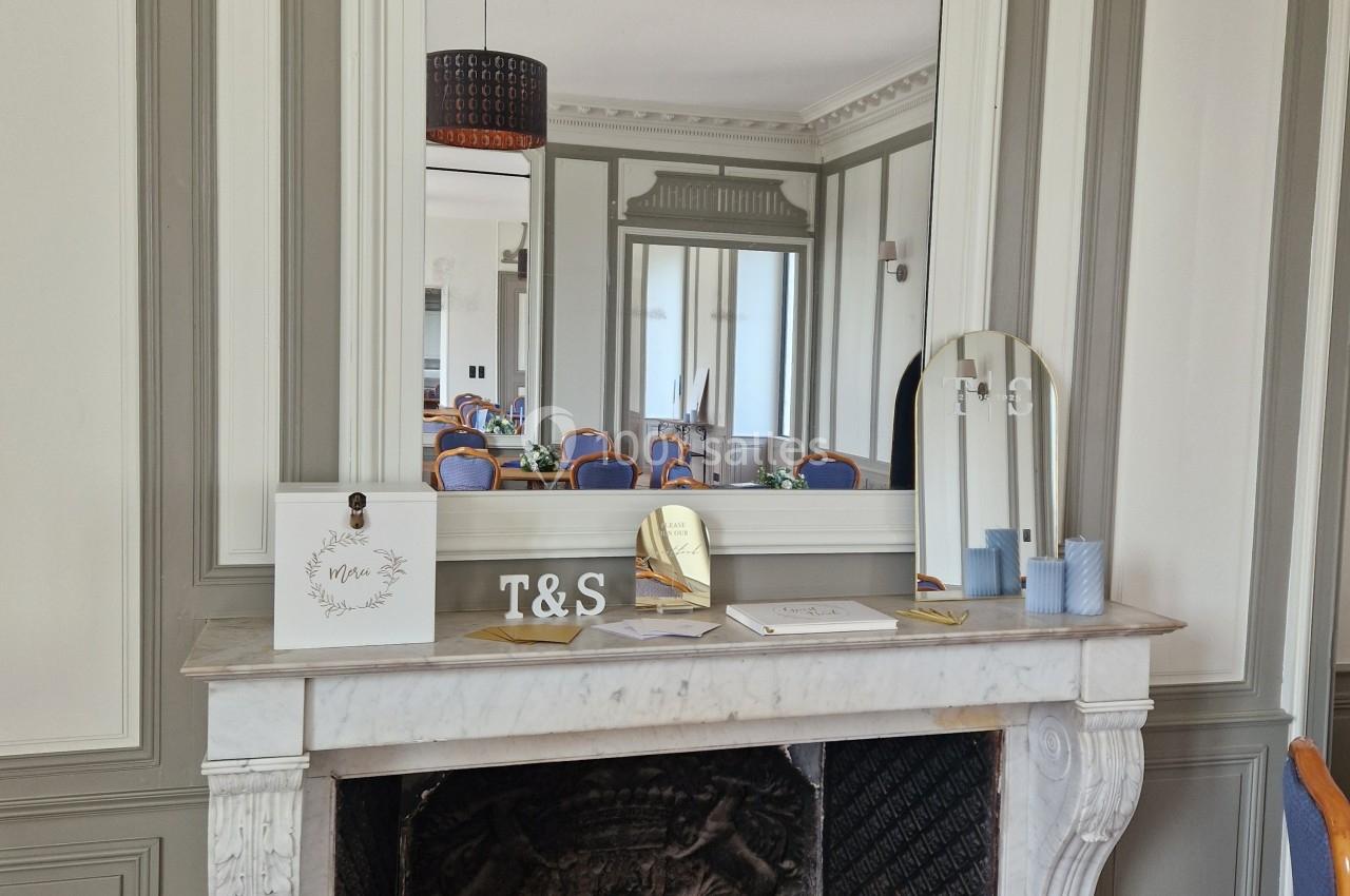 Cheminée décorative en marbre blanc surmontée d'un grand miroir, avec des objets posés sur le manteau.