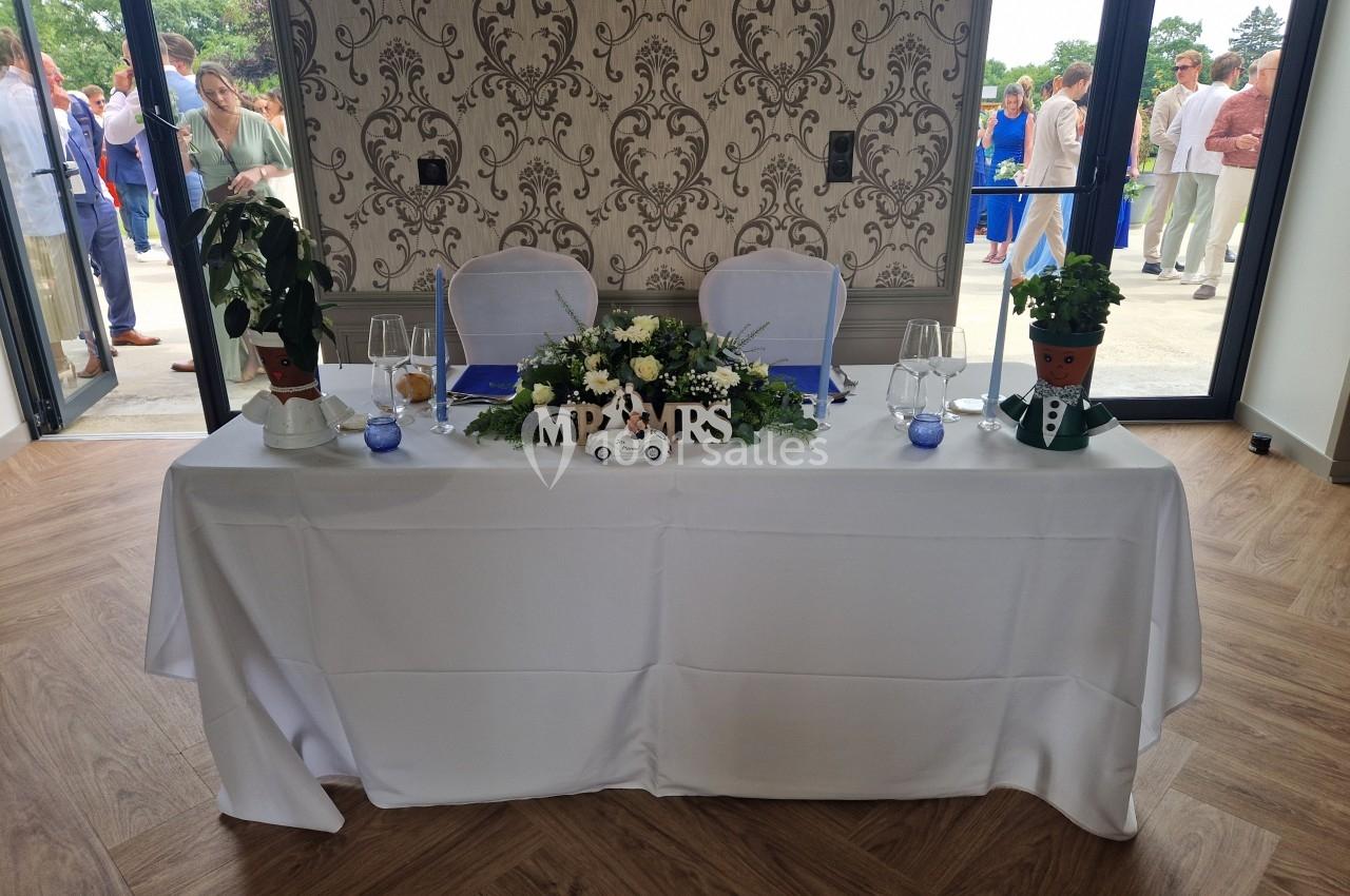 Table décorée pour un mariage avec fleurs, bougies et pancarte ’Mr & Mrs’, située devant un mur à motifs.