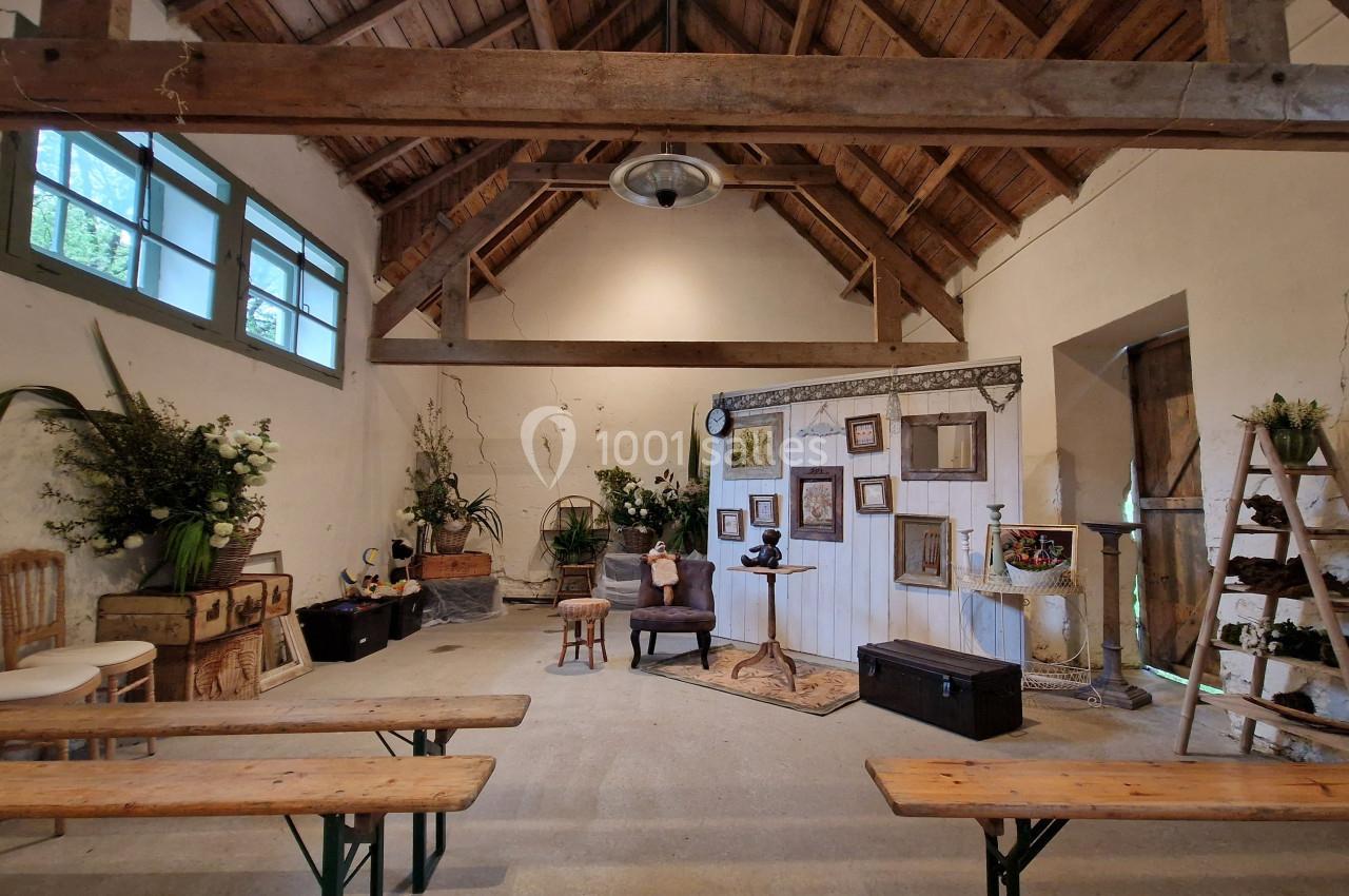 Salle rustique aménagée avec des bancs en bois, des décorations florales et des cadres accrochés sur un mur blanc.