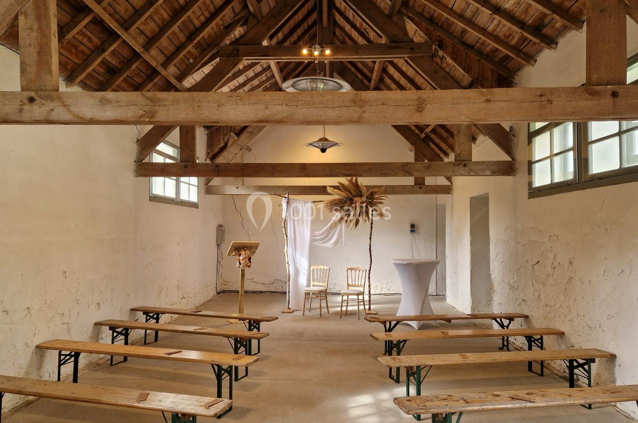 Intérieur d'une petite salle rustique avec bancs en bois, décorée pour une cérémonie avec deux chaises et un pupitre.
