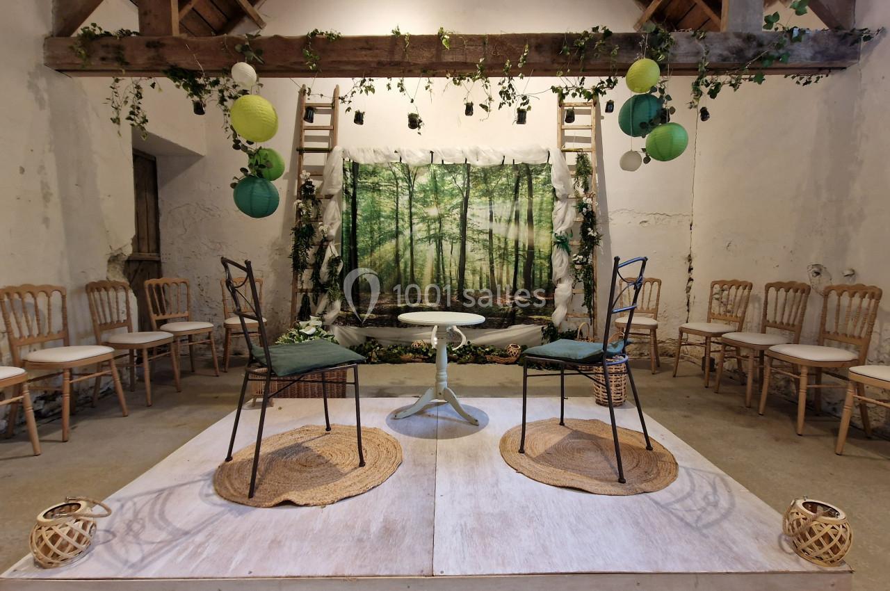 Deux chaises sur une scène décorée de lanternes, guirlandes végétales et fond représentant une forêt.