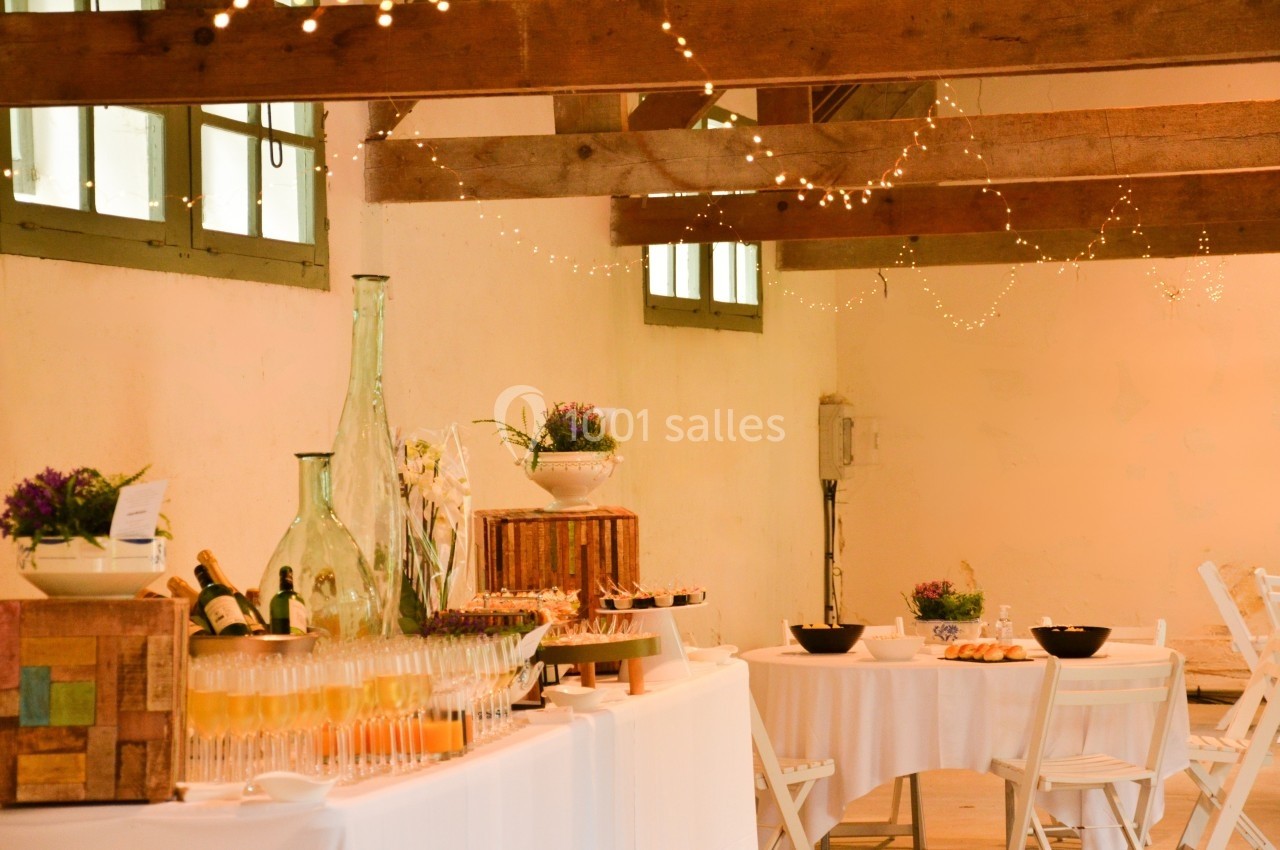 Table de réception décorée avec des boissons, des fleurs et des plats, dans une salle lumineuse avec poutres apparentes.
