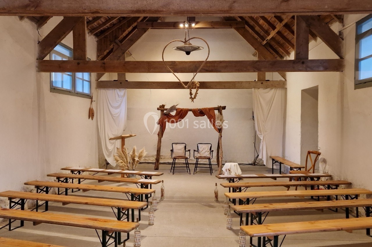 Salle rustique avec bancs en bois, décorée de rideaux blancs et d'un arche en bois ornée de fleurs séchées.