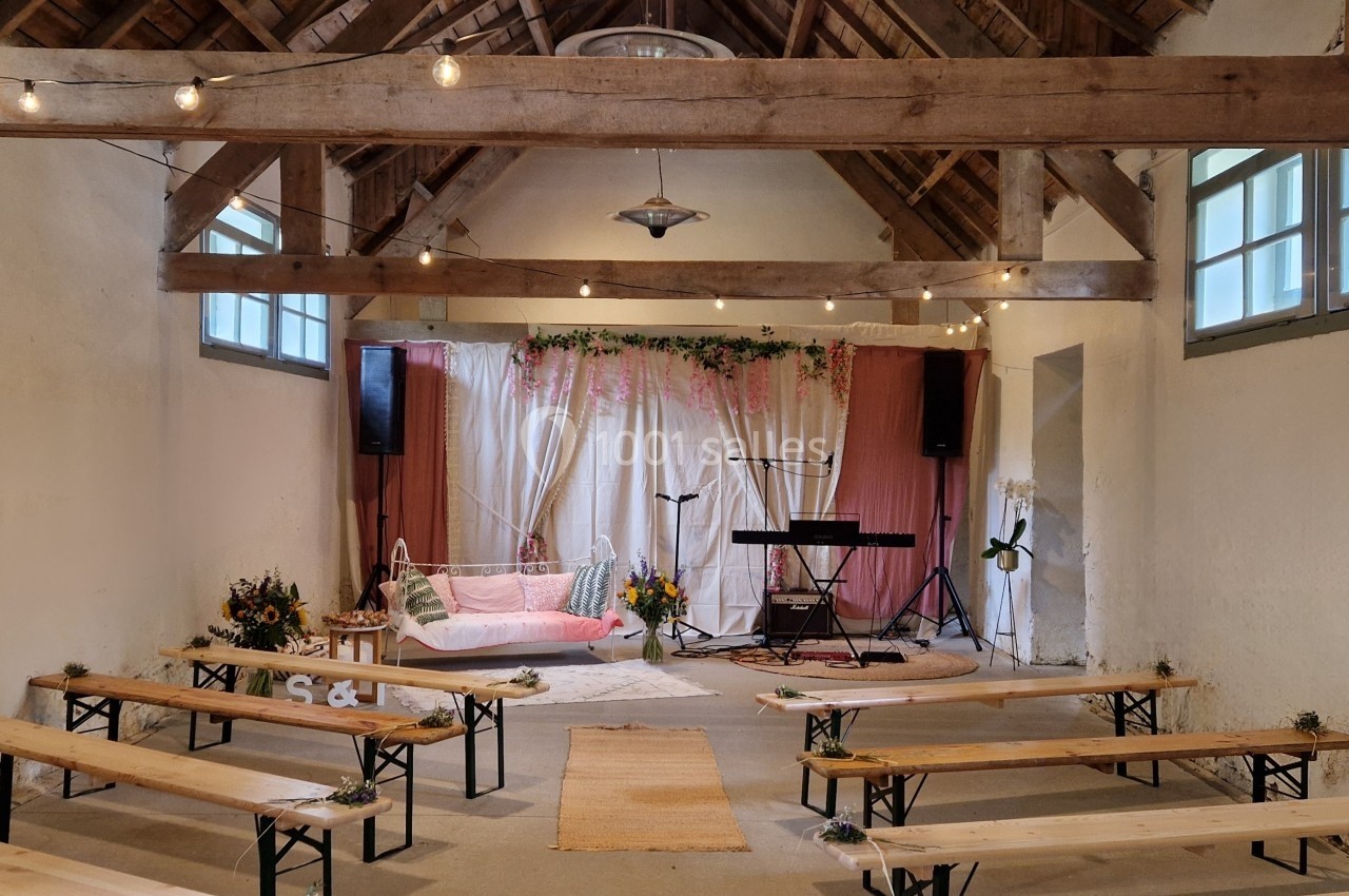 Salle décorée pour un événement avec bancs en bois, guirlandes lumineuses, rideaux roses et espace musical.