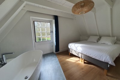 Chambre lumineuse avec un lit double, un mur bleu, une fenêtre avec rideaux jaunes et une porte en bois.