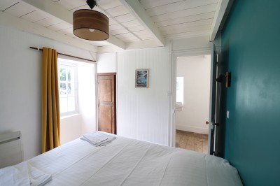 Chambre lumineuse avec un lit double, un mur bleu, une fenêtre avec rideaux jaunes et une porte en bois.