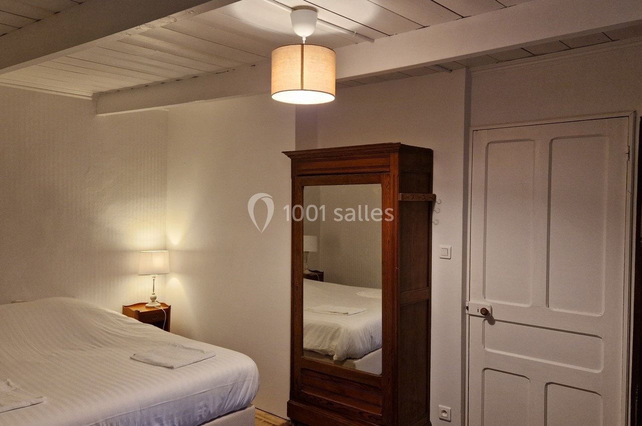 Chambre lumineuse avec lit double, armoire en bois avec miroir, lampe de chevet et plafond en bois peint.