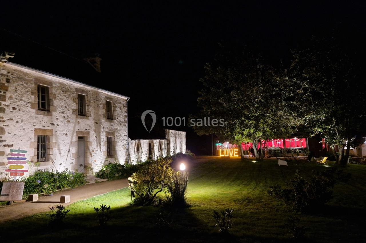 Bâtiment en pierre éclairé la nuit, avec un jardin et des lettres lumineuses formant ’LOVE’ en arrière-plan.
