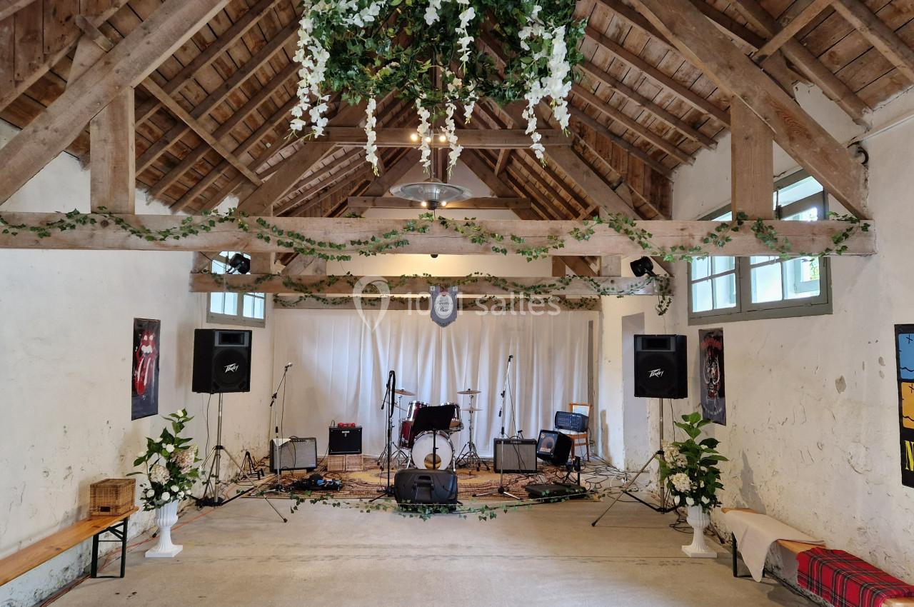 Salle rustique décorée de guirlandes végétales, avec une scène équipée d'instruments de musique et de matériel audio.