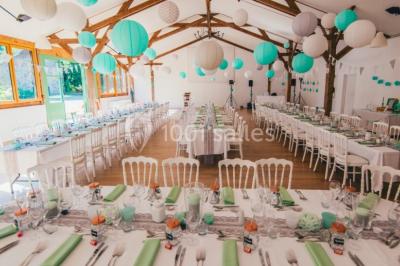 Salle de réception décorée avec des guirlandes lumineuses, remplie d'invités assis à des tables lors d'un événement.