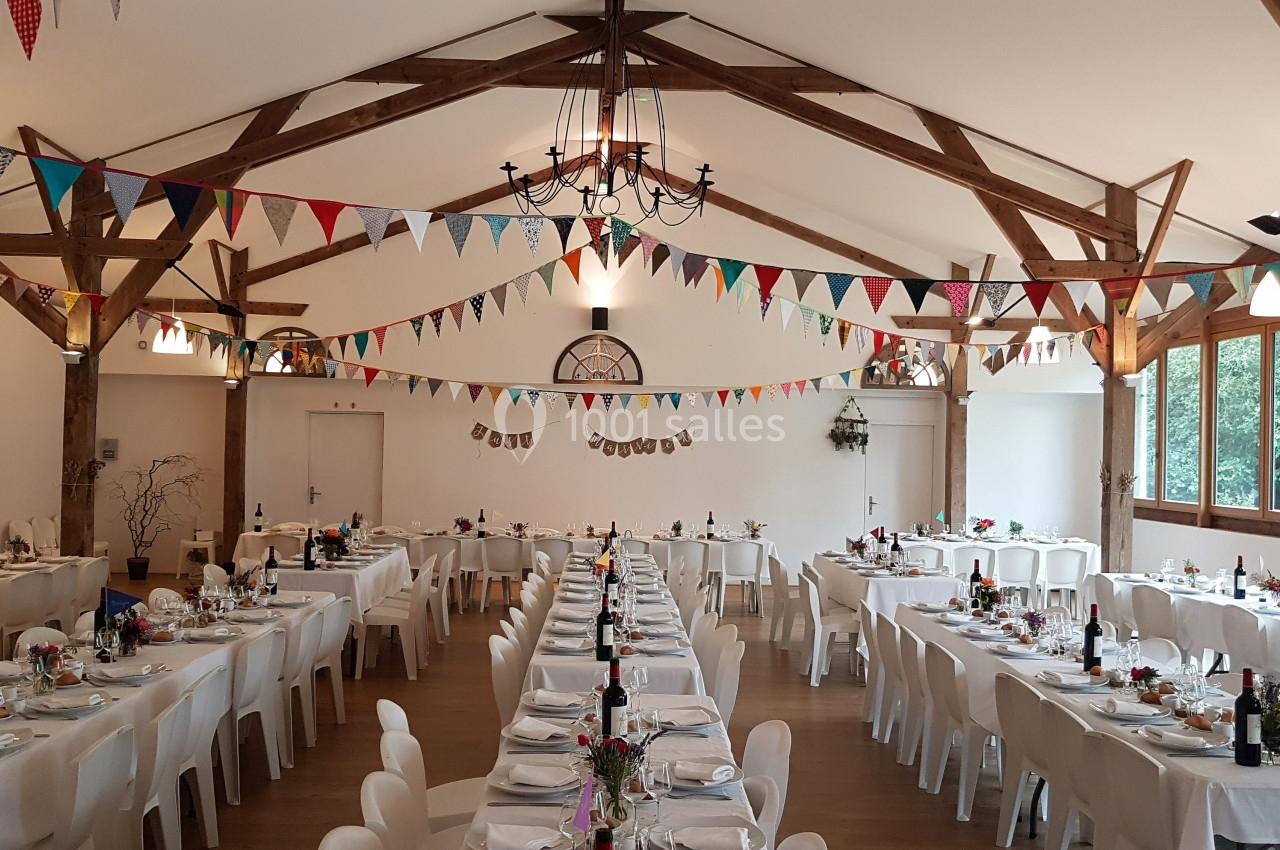 Salle de réception décorée avec des guirlandes colorées, tables dressées pour un événement festif.