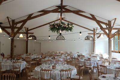 Salle de réception décorée avec des guirlandes lumineuses, remplie d'invités assis à des tables lors d'un événement.