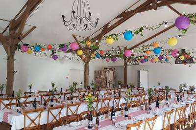 Salle de réception décorée avec des guirlandes lumineuses, remplie d'invités assis à des tables lors d'un événement.