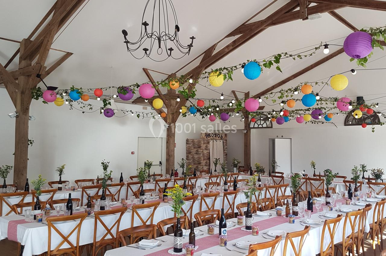 Salle de réception décorée avec des guirlandes lumineuses, lanternes colorées et tables dressées pour un événement.