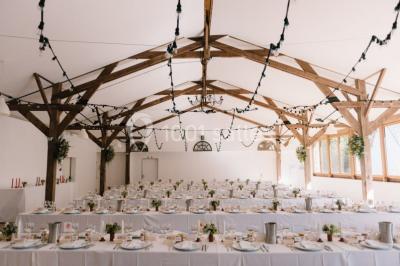 Salle de réception décorée avec des guirlandes lumineuses, remplie d'invités assis à des tables lors d'un événement.