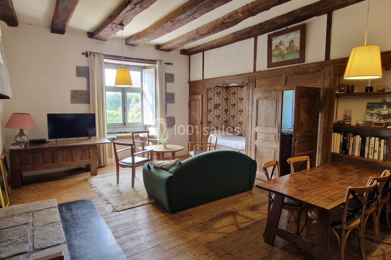 Salon rustique avec poutres apparentes, mobilier en bois, canapé vert, bibliothèque et cheminée en pierre.