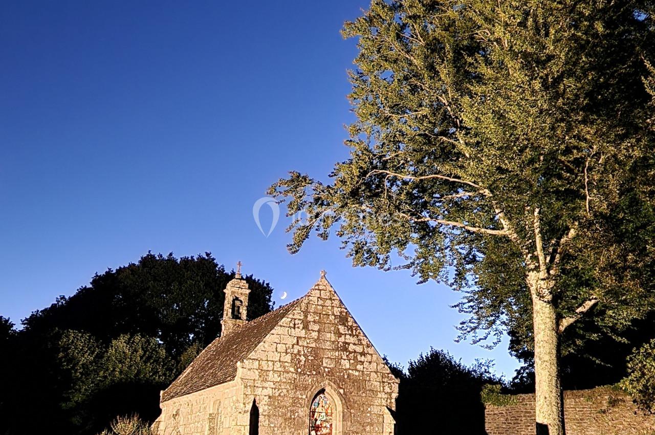Une petite chapelle en pierre éclairée par une lumière chaude, entourée d'arbres sous un ciel bleu profond.