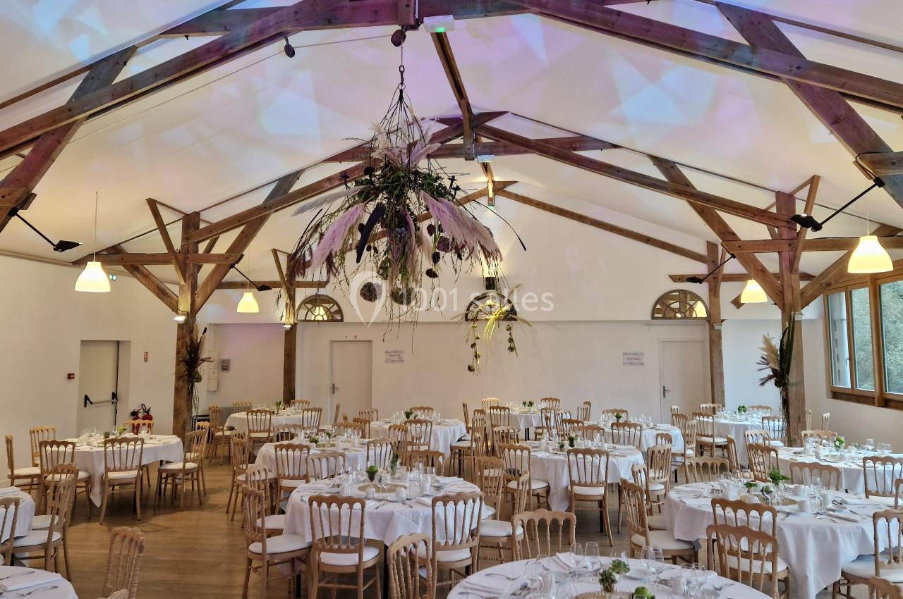 Salle de réception décorée avec des tables rondes dressées, des chaises en bois et une grande suspension florale.