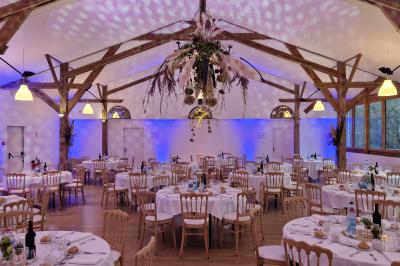 Salle de réception décorée avec des guirlandes lumineuses, remplie d'invités assis à des tables lors d'un événement.