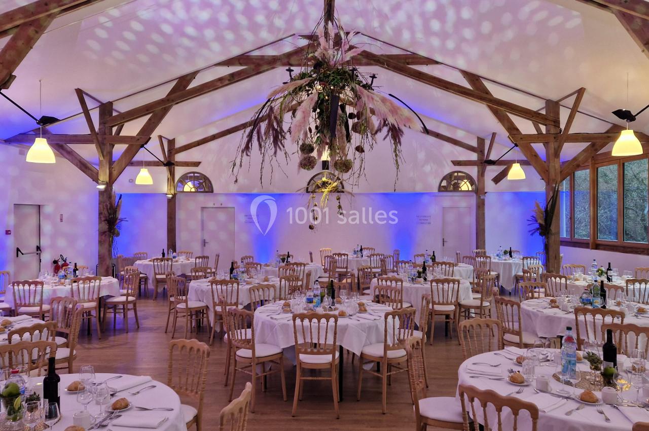 Salle de réception décorée avec des tables rondes dressées, un éclairage tamisé et une suspension florale centrale.