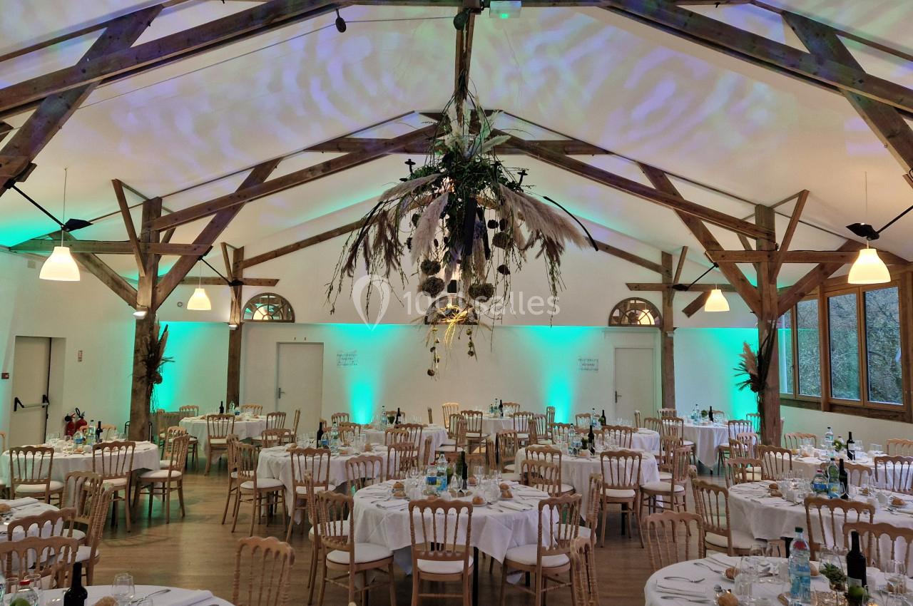 Salle de réception décorée avec des tables dressées, des chaises en bois et un éclairage tamisé aux tons verts.