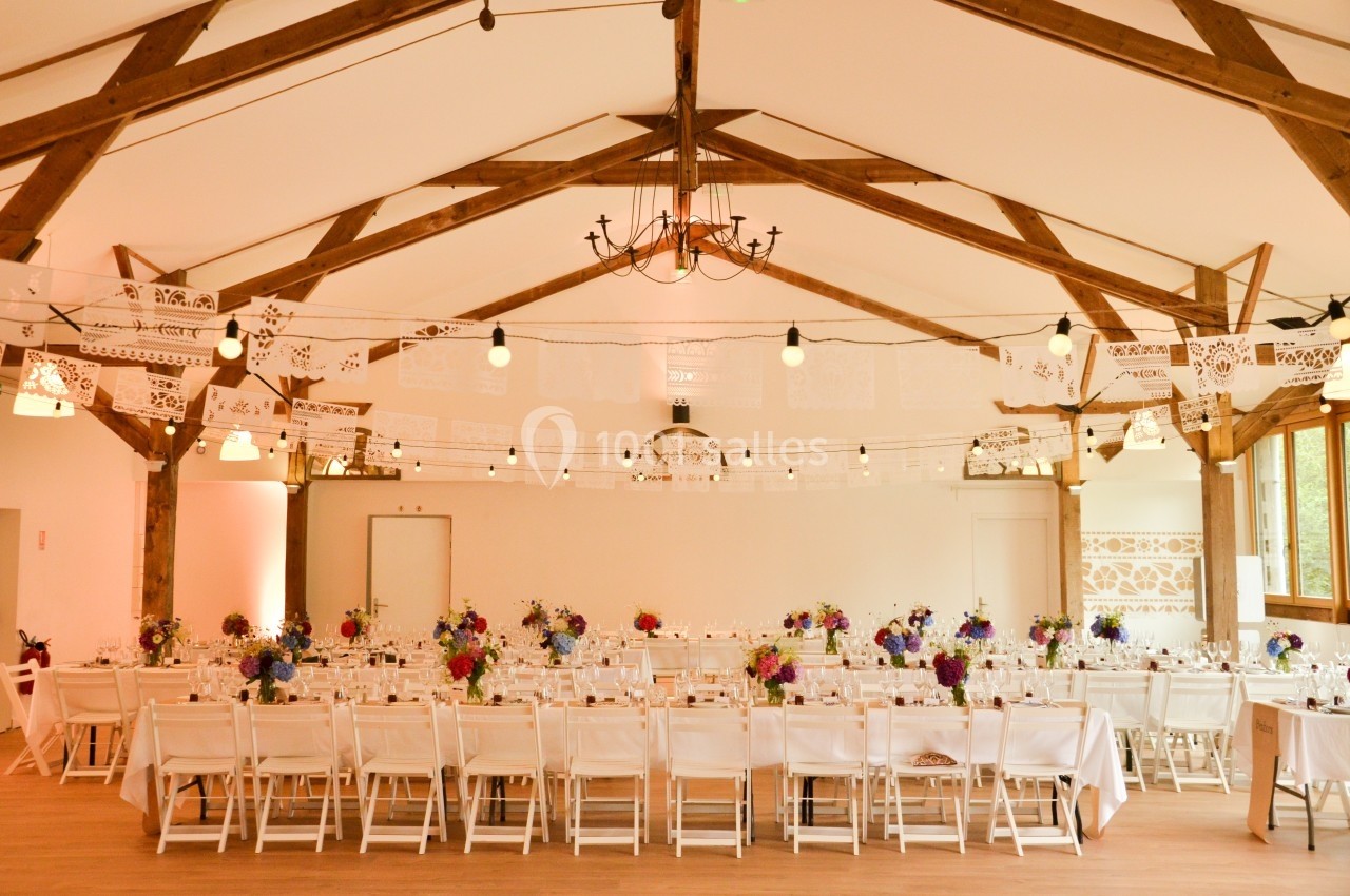 Salle de réception décorée avec des guirlandes en papier, des tables alignées et des bouquets de fleurs colorées.