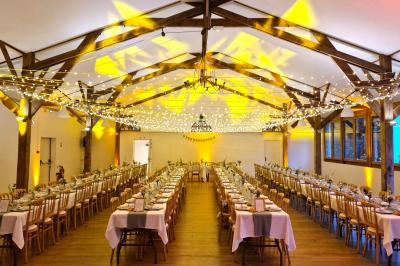 Salle de réception décorée avec des guirlandes lumineuses, remplie d'invités assis à des tables lors d'un événement.