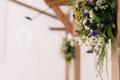 Salle de réception décorée avec des guirlandes lumineuses, remplie d'invités assis à des tables lors d'un événement.