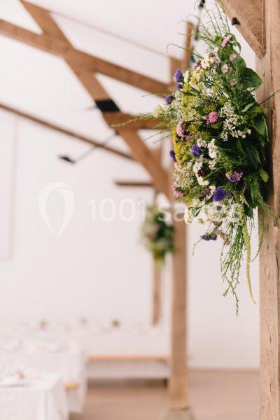 Décoration florale suspendue avec des fleurs sauvages colorées dans une salle lumineuse aux poutres en bois.