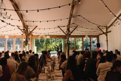 Salle de réception décorée avec des guirlandes lumineuses, remplie d'invités assis à des tables lors d'un événement.