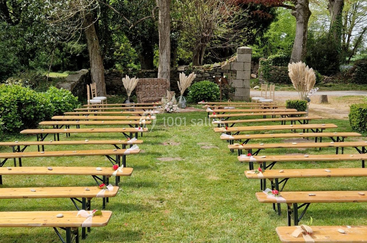 Allée centrale bordée de bancs en bois, décorée pour une cérémonie en extérieur dans un jardin verdoyant.