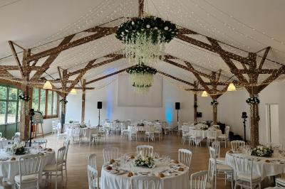 Salle de réception décorée avec des guirlandes lumineuses, remplie d'invités assis à des tables lors d'un événement.